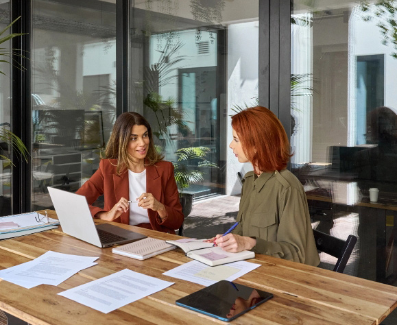 Two business women talking in creative office sitting at desk