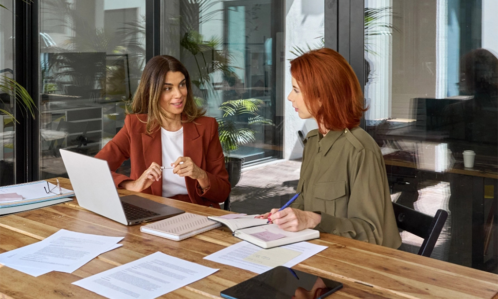 Two business women talking in creative office sitting at desk