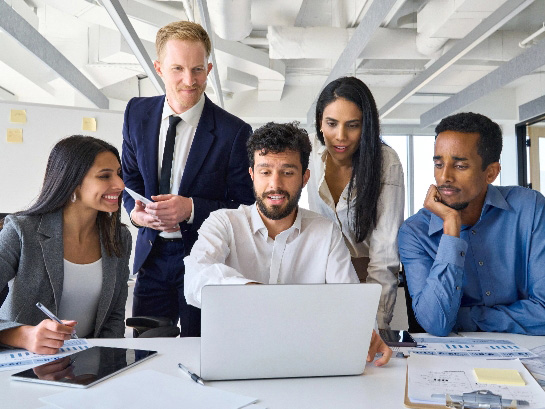 Group of diverse office workers looking at laptop in boardroom